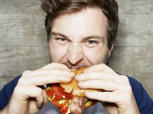 Мужчина с аппетитом поедает жирную еду, чтобы похудеть на кето диете.